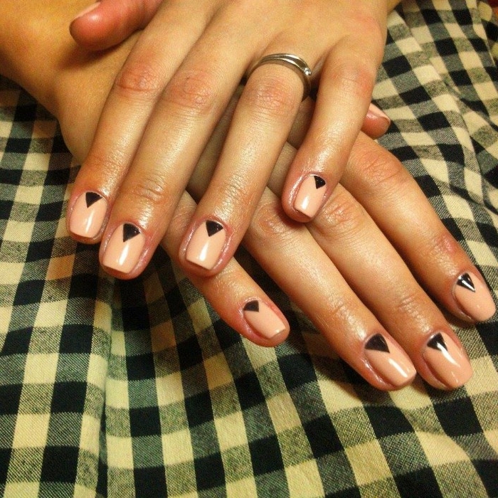 checkered fabric in white and blue, under two hands, with short nails, painted in nude pink, and decorated with small black triangles