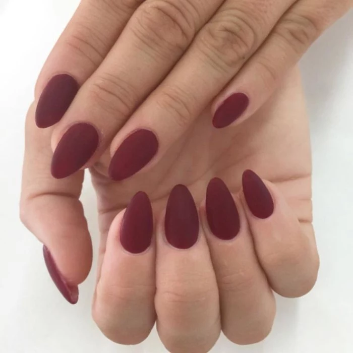 oxblood matte nail polish, on the short, pointy nails of two hands, seen in a close up, manicure ideas