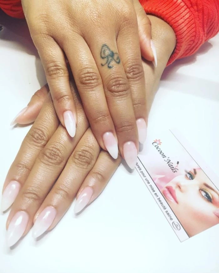 brown hands with pointy nails, painted in a pale, french manicure style, resting on a white surface