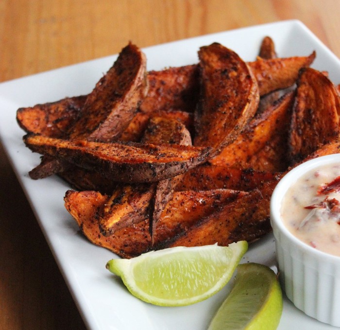 sweet potato wedges, seasoned with spices, and placed on a white ceramic dish, near a bowl with sauce, and two lemon wedges, hor d oeuvres