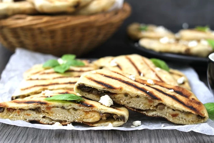 grilled flatbreads stuffed with vegetables, and peppered with white cheese, and fresh basil leaves, hor d oeuvres, placed on a white paper napkin