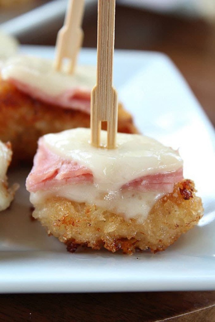 close up of a hot appetizer, consisting of grilled cheese and ham, skewered with a wooden fork