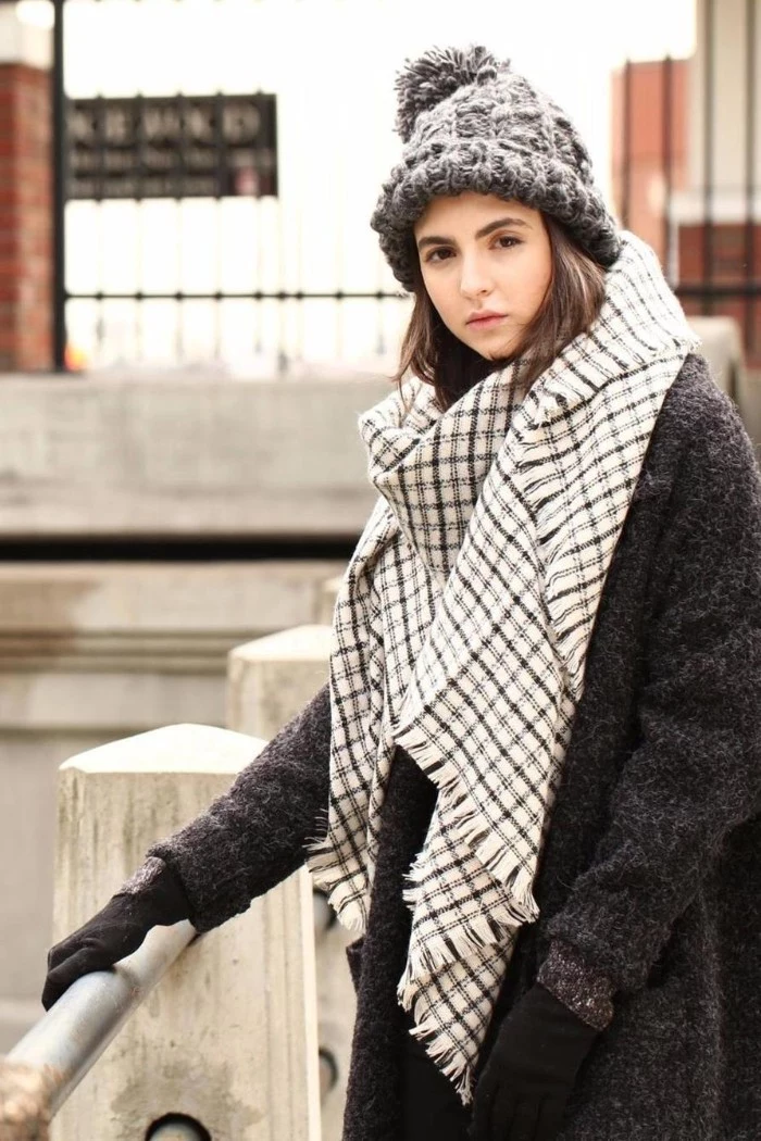 blanket shawl, in white and grey, worn by a young, brunette woman in a dark grey woolen coat, with a light grey, chunky knit beanie hat