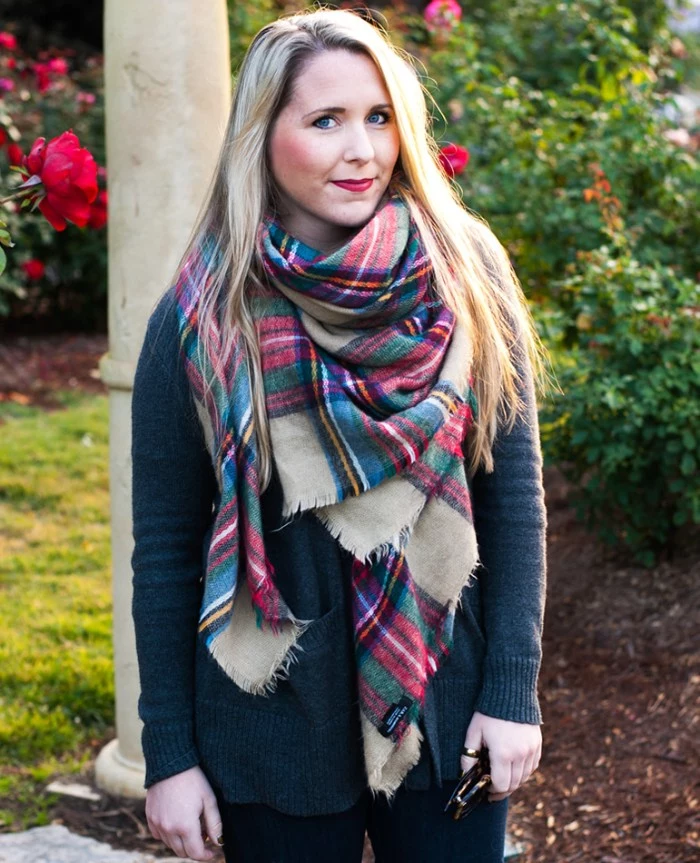 scarf outfits for fall, smiling blonde woman, with red lipstick, wearing a dark grey jumper, with an oversized plaid shawl, around her neck