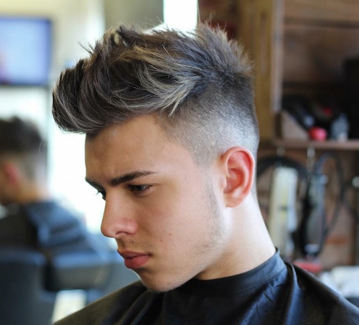 serious-looking young man, facing to one side, with a highlighted faux hawk, short haircuts for men, in a hairdresser's salon