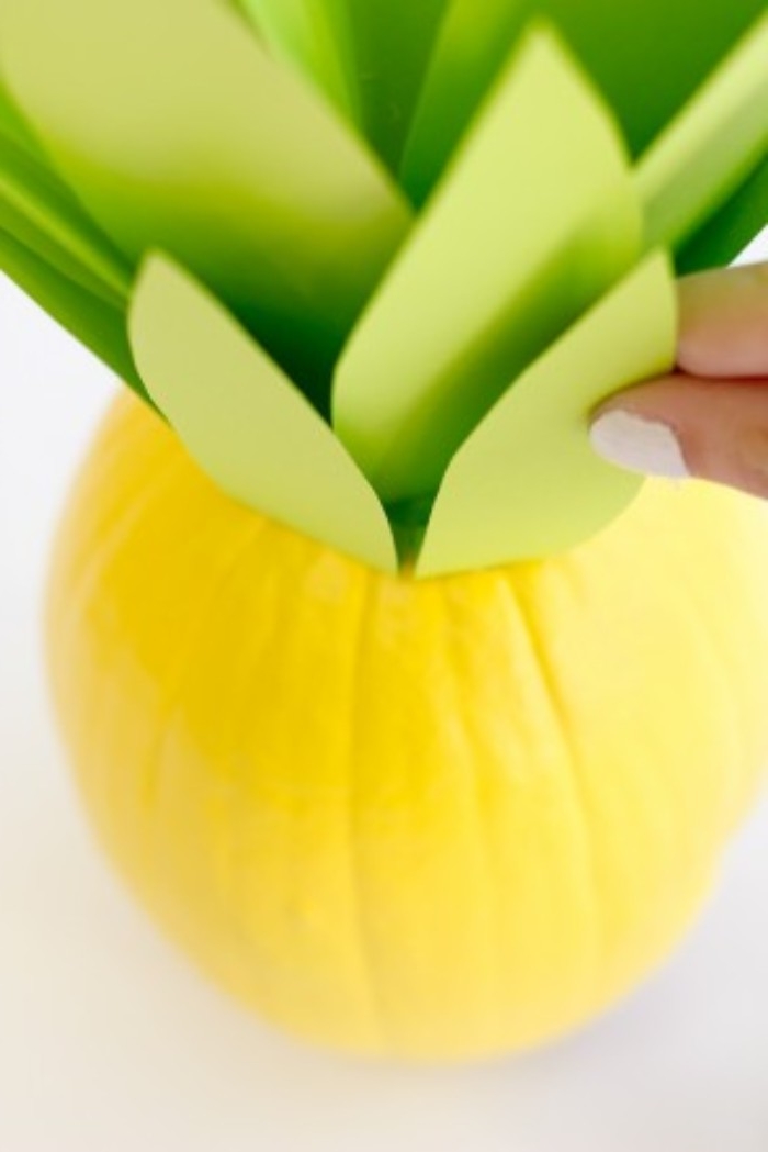 nail polish in white, on a hand attaching a small, leaf-shaped green paper cutout, to the top of a yellow pumpkin, how to decorate your room, with diy crafts