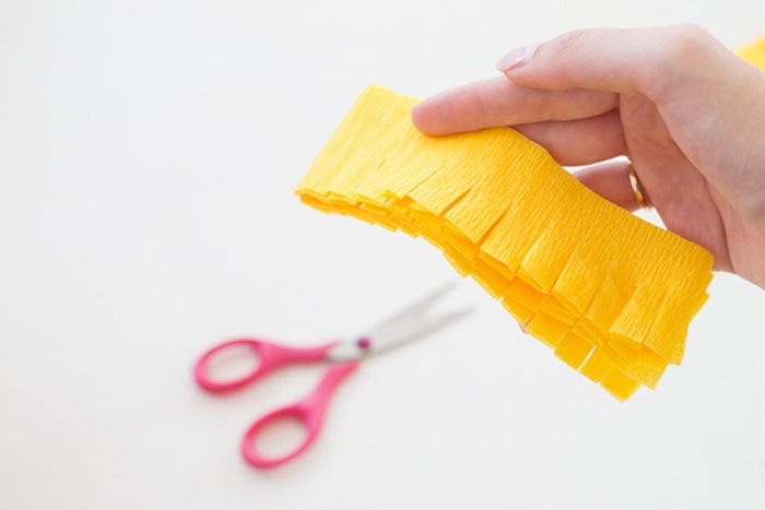 hand holding a piece of yellow tissue paper, folded several times, and featuring a few even cuts, couples halloween costumes diy, scissors in the background