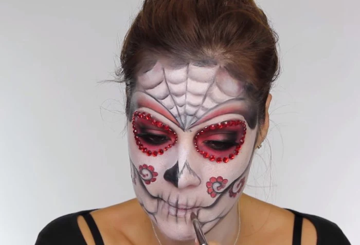 almost completed sugar skull makeup, halloween face paint, worn by a young woman, with brunette hair tied in a ponytail