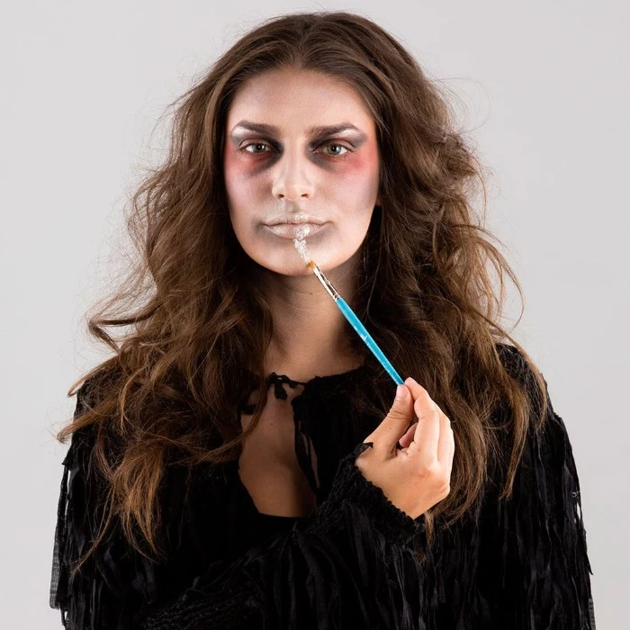 step by step photo tutorial, explaining how to create zombie face paint, young brunette woman, applying special effects makeup wax, on her lip, using a brush 