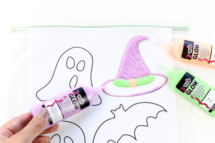 painting over a clear ziplog bag, containing a white sheet of paper, with simple halloween shapes, using a tub of purple paint, halloween party decoration ideas, glow-in-the-dark-stickers