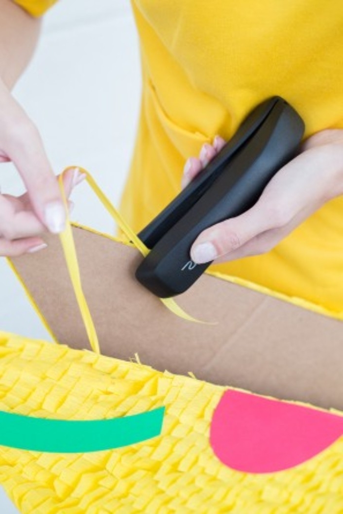 stapling a piece of yellow ribbon, on two decorated pieces of cardboard, using a black stapler, couples halloween costume ideas