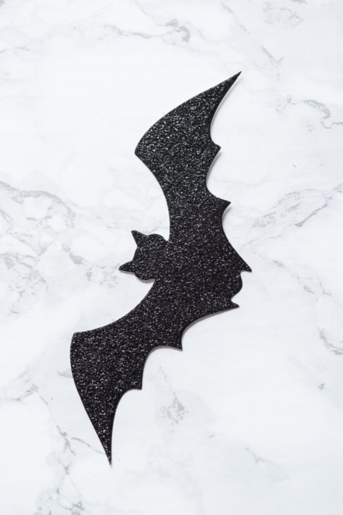 extreme close up, of a small bat shape, cut out from black glittering card, and placed on a marble surface