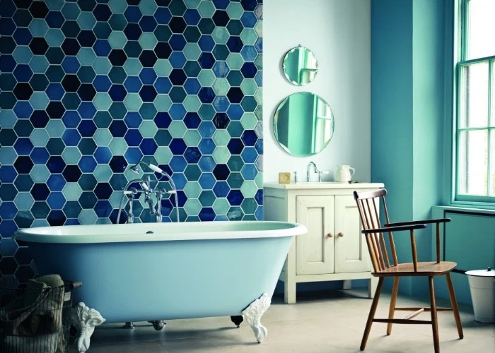 tiles in different shades of blue, with a beehive-like pattern, decorating the wall of a pale blue room, bathroom paint colors, vintage-style clawfoot bath