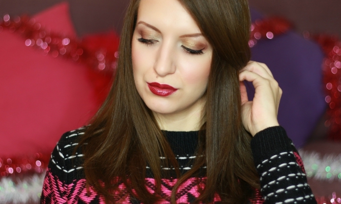festive sweater in black, white and pink, worn by a pale brunette woman, with dark red glossy lipstick, and christmas eyeshadow in shimmering beige