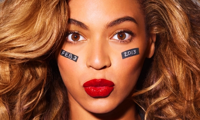 pouting expression made by beyonce, with caramel brown hair, red lipstick and black strips with white letters and numbers, on her cheeks