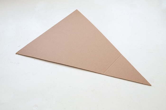 triangular piece of beige cardboard, for making a pizza costume, couples halloween costumes, placed on a pale grey surface
