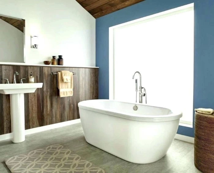 sink and bathtub in white, in a room with white walls, half-covered by dark brown wood paneling, aegean blue bathroom accent wall, pale grey laminate floor
