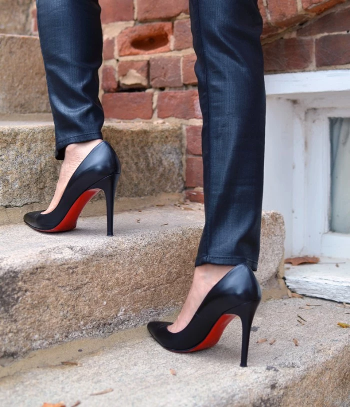 stilettos in black, with red soles, what is a capsule wardrobe, worn by two slim legs, dressed in dark blue jeans