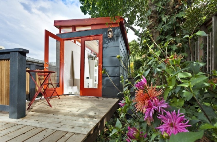 purple and orange flowers, in a garden, containing a blue and dark orange, modern she shed, small garden table, and a chair nearby