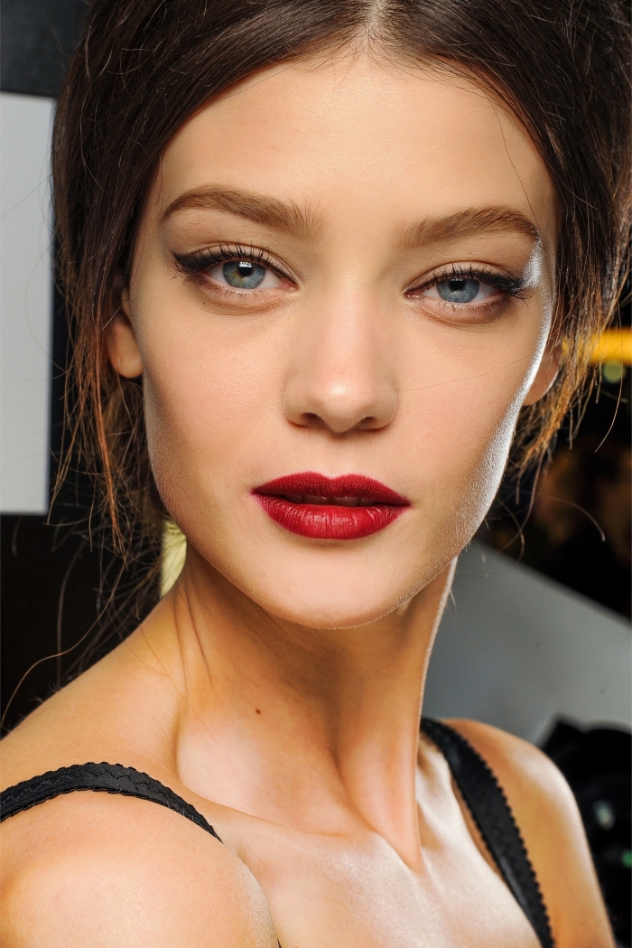 slim brunette female model, with blue eyes, wearing red lipstick, black mascara and eyeliner, holiday makeup 2017, in a black strappy top