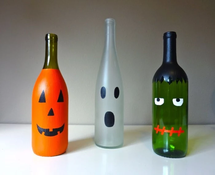 glass bottles painted like halloween monsters, an orange jack-o-lantern, a white ghost, and a green frankenstein's monster, halloween party decoration ideas