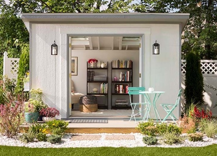 a set of brown shelves, inside a white shed, with open doors, she shed interiors, teal garden table, and two matching chairs nearby