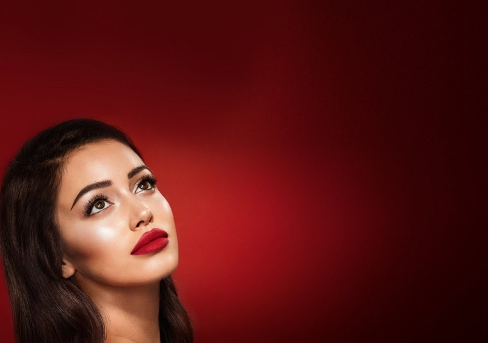 full lips with red lipstick, on a young brunette woman, with long dark hair, fake lashes and black mascara, christmas makeup, on a dark red background