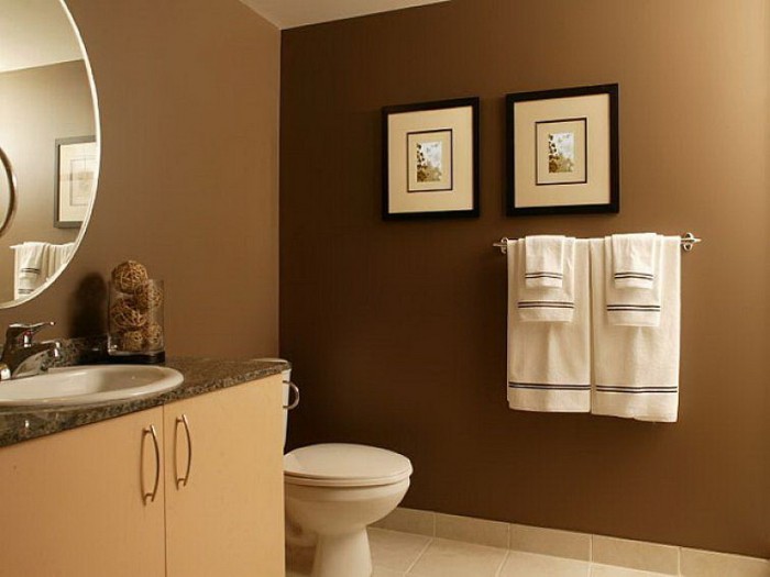 small bathroom paint colors, chocolate brown walls, decorated with a round mirror, and two framed artworks, pale beige cupboard, with an inbuilt sink