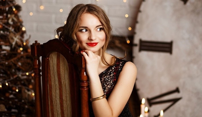 sequined black and silver dress, worn by a smiling young woman, with wavy brunette hair, and red lipstick, sitting on a chair