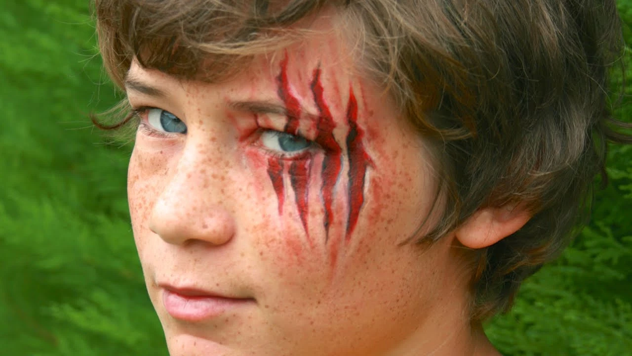 slashed eye wound, realistic claw marks face paint, worn by a young boy, with wavy brunette hair, blue eyes and freckles