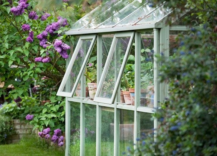 orangery building made of glass, with white frames, two open windows, various potted plants visible inside