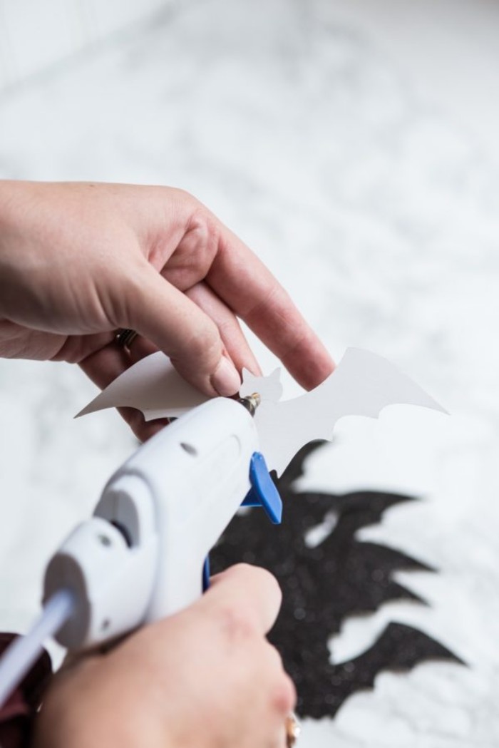 person pouring glue on the back, of a bat-shaped cutout, using a glue gun, more bat shapes in the background