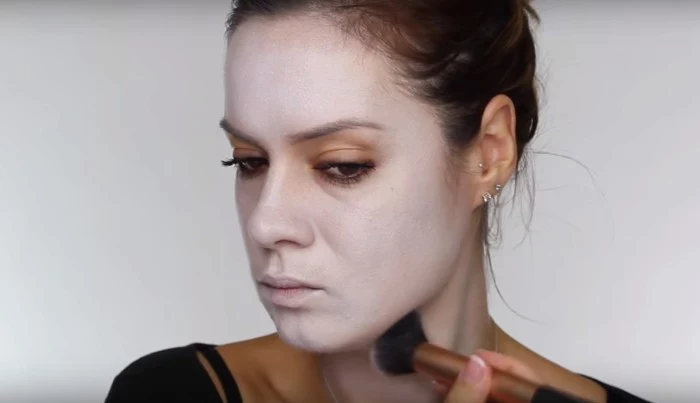 woman applying white powder on her face, using a brush, how to create skeleton face paint, tutorial with photos
