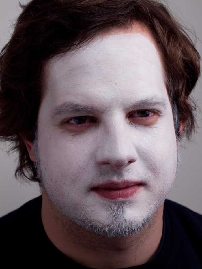 short beard worn by a smiling brunette man, entire face covered in white paint, clown face paint