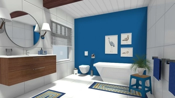 round mirror on a white paneled wall, inside a spacious room, with a cobalt blue bathroom accent wall, three framed images of birds, a bathtub and a small blue stool