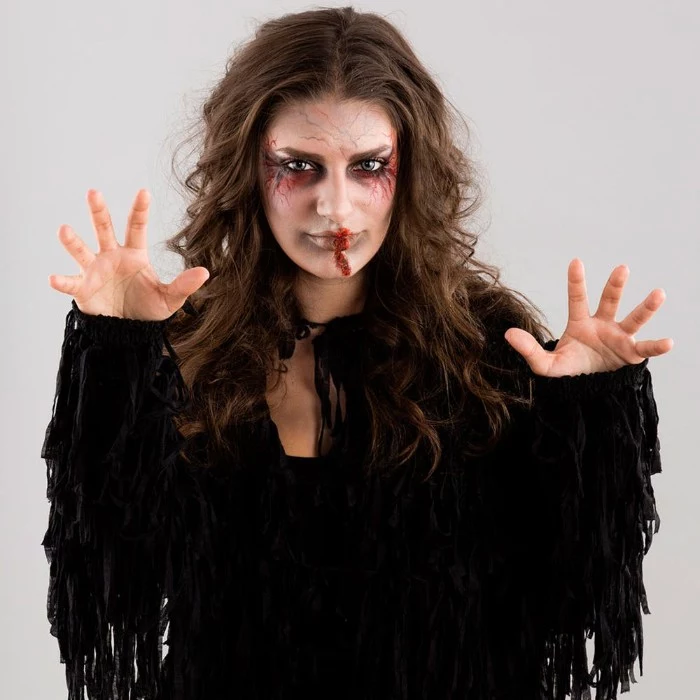 black costume with tassels, worn by a brunette woman, with messy and wavy, long brunette hair, and halloween face paint, featuring fake blood