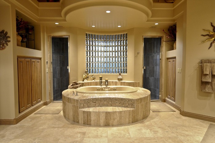 symmetrical room with an elevated bath at the center, two shower cabins, beige tiled floor, spa like bathrooms, wooden cupboards and decorations