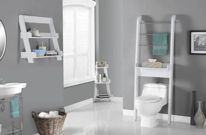 towel rack in white, placed over a white toilet, in a bathroom with medium grey walls, and a shiny white floor, window and shelves with toiletries