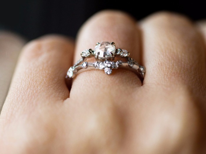 split shank silver or platinum ring, featuring one large white diamond, and several small white diamonds, on a person's hand, seen in close up