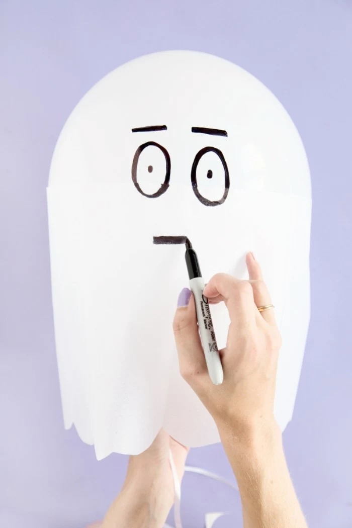 face drawn with black permanent marker, on a white balloon, decorated with white paper, to look like a ghost