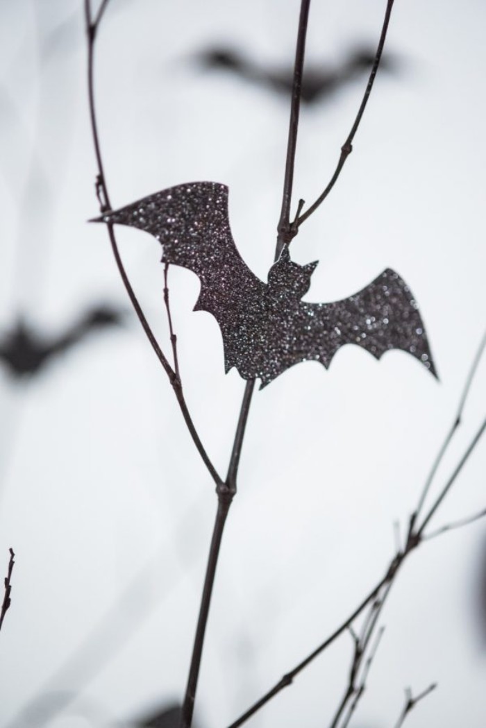 close up of a thin branch, decorated with a small, glittering bat shape, cut out from black card