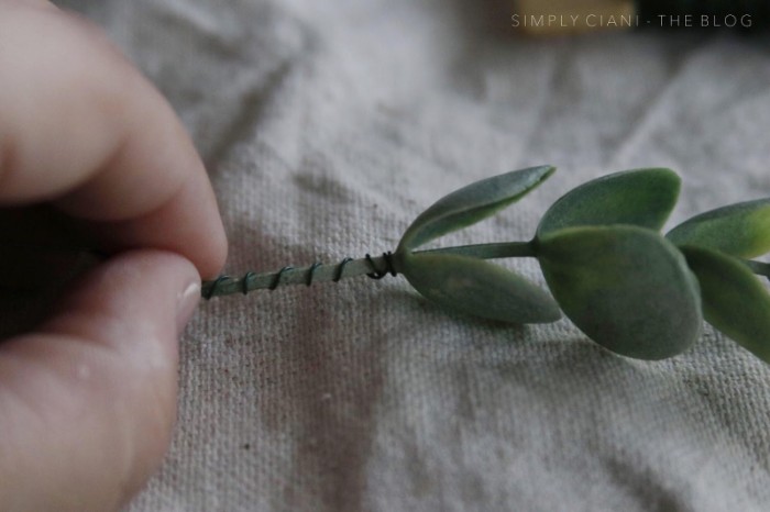 wire wrapped around the stalk, of a small green plastic plant, held by a pale hand, dollar store crafts, seen in extreme close up