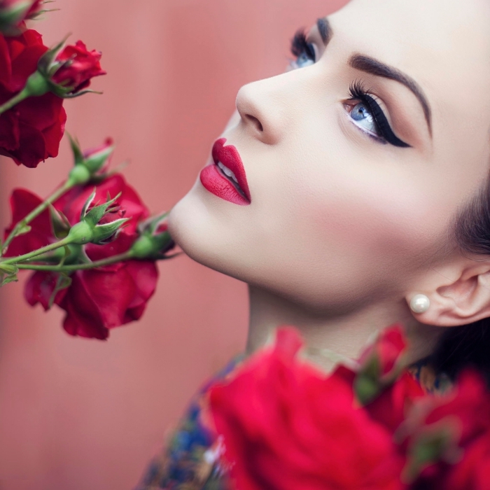 bold black eyeliner, worn by a pale young woman, with glossy red lipstick, and pale pink blush, christmas makeup, several red roses nearby