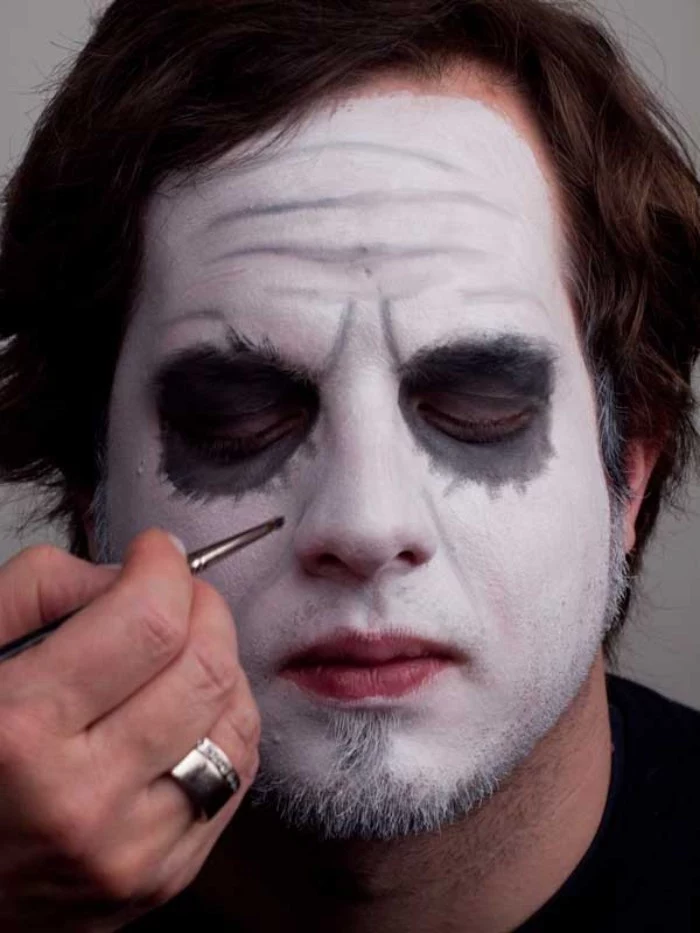 lots of wrinkles, painted with grey, on the face of a young man, wearing white makeup, and grey eyeshadow around his eyes, clown face paint, batman joker look