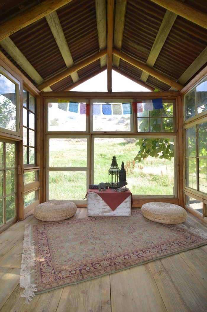 rug with faded ornamental pattern, and white tassels, inside a wooden she shed, with lots of windows
