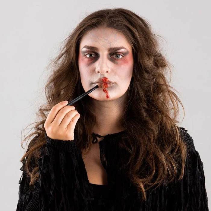 faux blood added with a brush, on a the lips of a woman, with zombie face paint, wearing a black costume