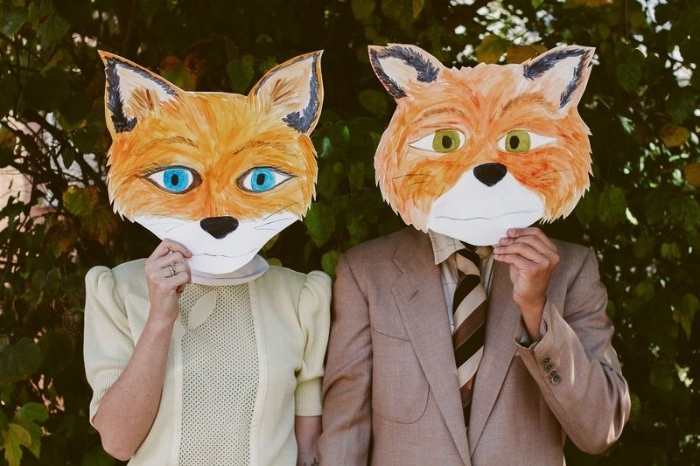 hand-painted paper masks, of fantastic mr. fox, and mrs fox, held in front of the faces of a man and a woman, quick halloween costumes, inspired by wes anderson