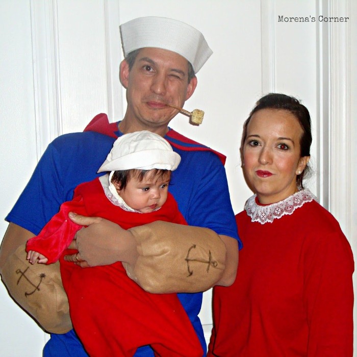 family dressed like characters from popeye the sailor, man with a pipe, wearing a sailor's uniform, and holding a baby, next to him is a woman, dressed like olive oyl
