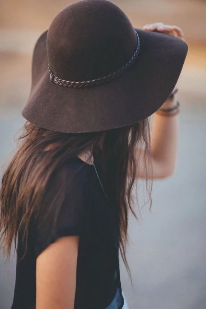 large dark brown felt hat, with woven leather detail, worn by a brunette woman, with long hair, and a black t-shirt