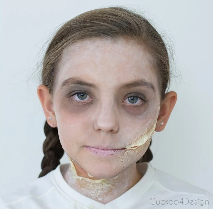 t-shirt in white, worn by a young girl, with face covered in white powder, fake scars on her cheek and neck, scary face paint, grey eye shadow around her eyes